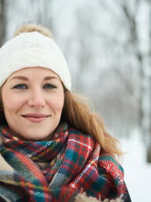Portrait on an attractive female solo traveler wearing a white tuque in a snow filled winter forest in Canada