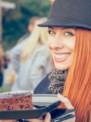 Cute happy woman in a hat eating a cake outdoors
