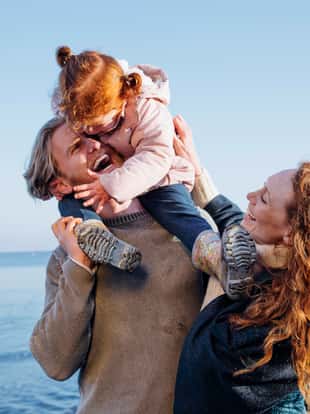 Young couple enjoying walking along the coast. Its cold outside so they are wrapped up warm. The man is carrying a little girl on his shoulders
