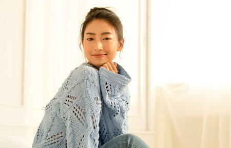 Portrait of beautiful young Asian woman smilling friendly and looking at camera in living room at home on a bright winter morning. Concept woman lifestyle and winter. Autumn, winter season.