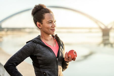 Happy African American Athletic Woman Eating An Apple After Exercise.