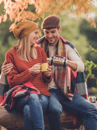 Happy couple enjoying in autumn day in the park while man is pouring coffee to his wife.