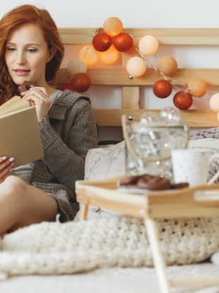 Young woman eating chocolate gingerbread cookies while reading a book