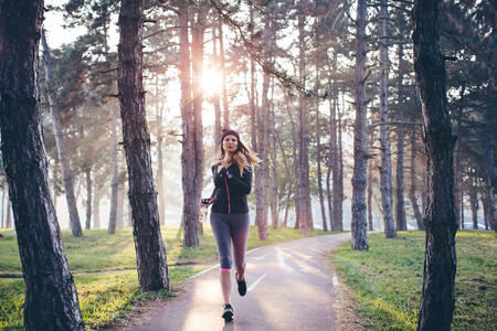 Young woman jogging outside in sunny autumn forest. The sun is shining in the background .