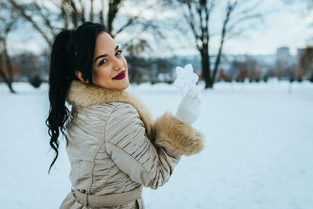 Portrait of a beautiful young woman holding a snowflake on a snowy winter day in the city park