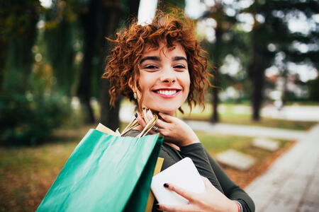 Young redhead shopping woman holding shopping bags at public park
