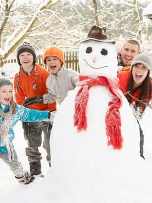Family Having Fun Building Snowman In Garden