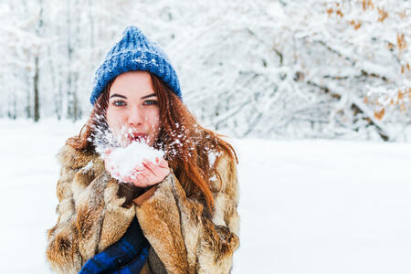 charming young woman in blue knitted hat blowing on snow. active walk in winter