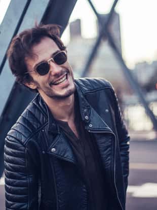 Young and handsome modern man enjoys a lovely day out in the city. He is standing on a bridge.
