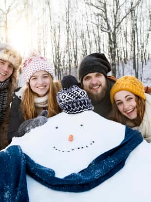Group of young friends posing for photo with snowman in winter nature.