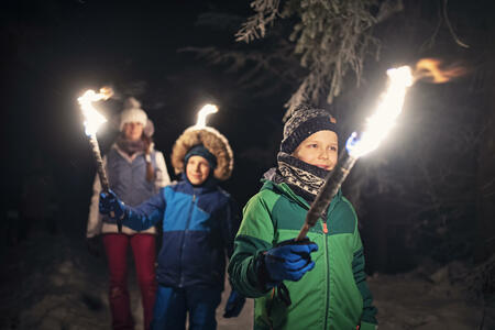 Three kids hiking in beautiful winter forest at night. Kids are holding flaming torches.Nikon D850