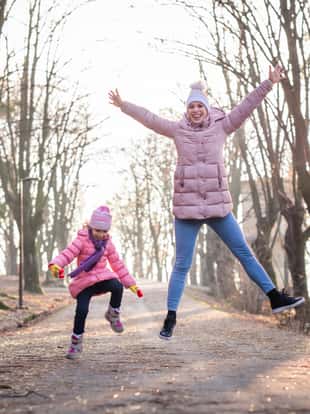 Mother and daughter having fun while jumping outdoors.