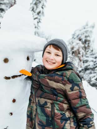 boy making a snowman outside, in a park, during winter month