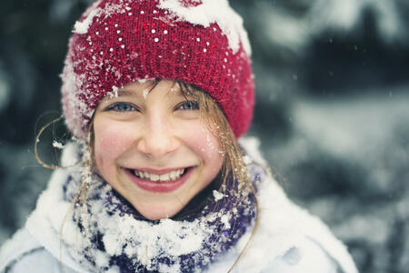 Winter portrait of a beautiful little girl laughing and having a lot of fun in snow. The girl aged 8 and her scarf, face and cap are snow covered. Some of the snow have melted on her cheeks.