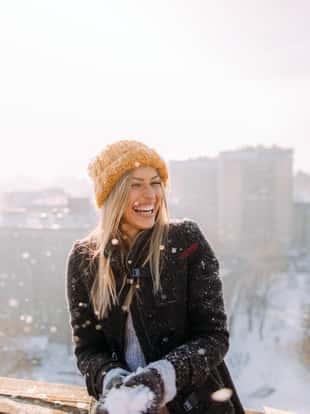 Young smiling woman enjoys snowy winter day on a rooftop terrace that overlooks the city