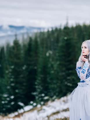 groom in a blue suit and bride in white, embroidered with blue pattern, dress on a background of green pine forests in the mountains of the Carpathians