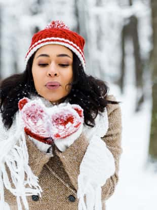 beautiful african american woman blowing snow in winter forest