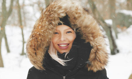 A happy blonde woman in a parka with a hoodie on a windy winter day in Sweden.