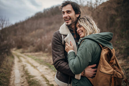 Man and woman, beautiful young couple hiking together and hugging in nature on a winter day.