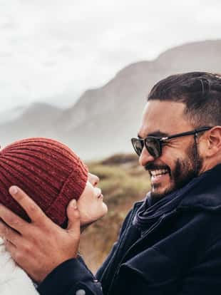 Close up portrait of loving couple in warm clothing outdoors. Side view of smiling man and woman enjoying a winter day at the beach.