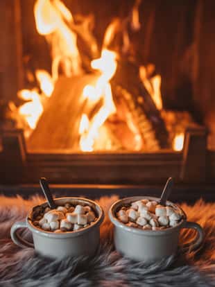 Cups with hot chocolate on fur, fireplace in background