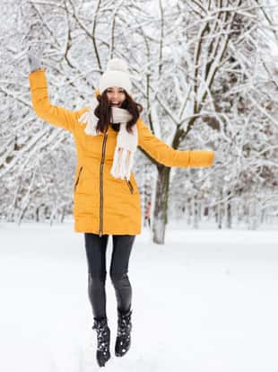 Full-length shot of joyful brunette lady playing and running while walking in snow park
