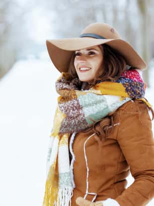 happy elegant woman in brown hat and scarf outside in the city park in winter in sheepskin coat.
