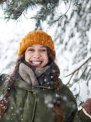 Waist up portrait of happy young woman posing outdoors in winter standing under beautiful pine trees, copy space