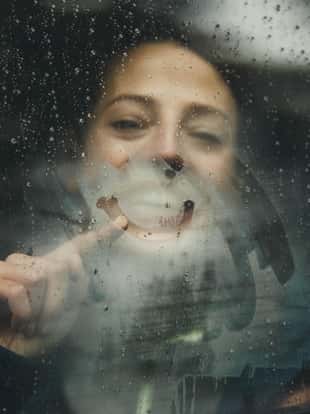 Close up of happy woman drawing smiley face on foggy car window during rainy day.
