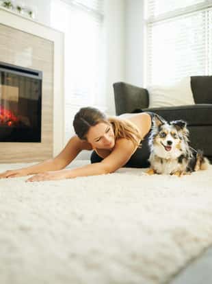 Shot of a young woman exercising at home with her dog keeping her company