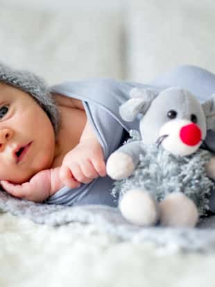Little newborn baby boy, looking curiously at camera, lay dawn in bed, holding little toy