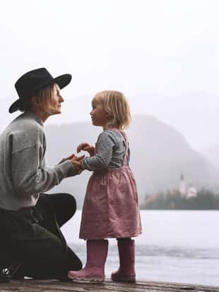 Mother and daughter looking at beautiful Lake Bled. Family travel in Slovenia, Europe. Boho style woman and little girl in nature outdoor near by lake on foggy day. Adventure time with kids in nature.