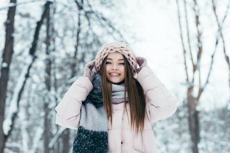 portrait of smiling woman in winter clothing looking at camera in snowy park