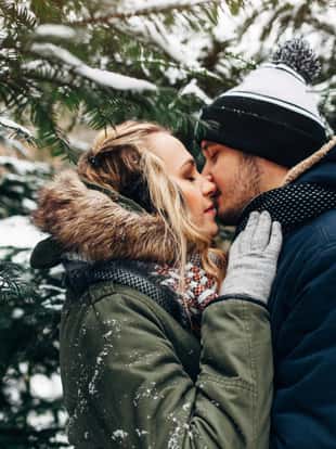 Portrait of young couple man and woman kissing in background of christmas tree with snow in winter Park