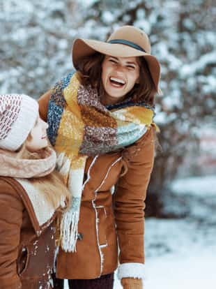 smiling stylish mother and daughter in hats and sheepskin coats with mittens outdoors in the city park in winter.