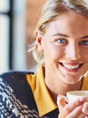 Portrait of smiling young woman holding coffee cup at home. Beautiful female is having refreshment during winter. She is wearing sweater.