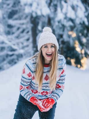 Woman on snow having real good time. She is throwing snowballs and enjoy in every moment in cold winter day.