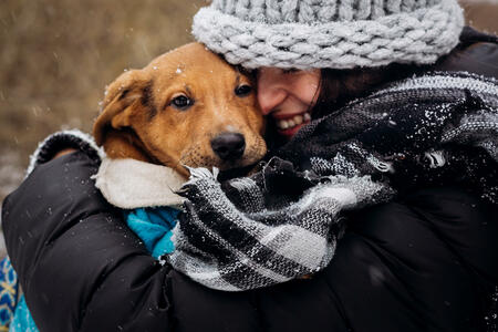 stylish hipster woman hugging and smiling cute puppy in snowy cold winter park. moments of true happiness. adoption concept. save animals