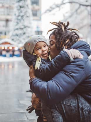 Young father with daughter walking on snowy street and enjoy in winter magic. They wearing warm clothing
