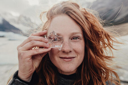 Red haired Girl looking through glacier ice in mountain backdrop on trip to el cheltan Argentina patagonia
