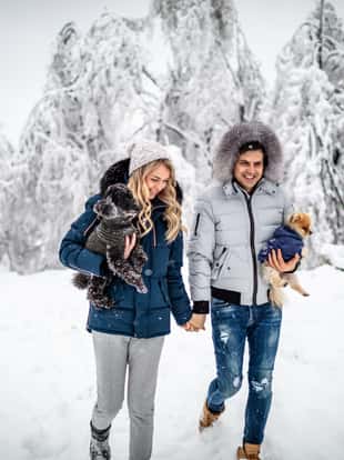 Photo of happy couple on a snow walking with their little dogs
