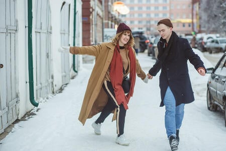 Young beautiful couple lovers hugging, laughing and has a fun winter time in a snow winter city. Winter holidays, love concept.