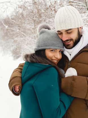Young boy in warm clothes hugging and warming up her girlfriend in winter forest