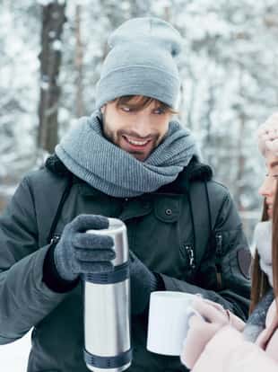 young couple drinking tea from thermos in winter park