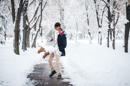 Young man is piggybacking his girlfriend in snowy public park.