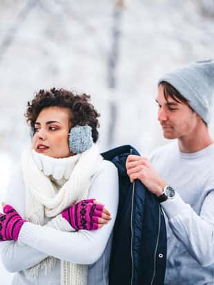 Young man warming girlfriend with his coat.