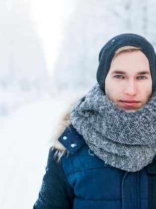Close up portrait of young man in snowy forest road, looking at camera.