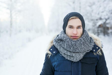 Close up portrait of young man in snowy forest road, looking at camera.