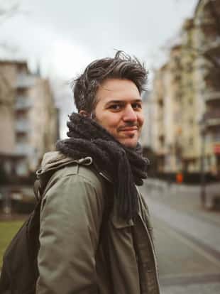Vintage toned portrait of a young man walking in Berlin, in the Schoneberg district of West Berlin, wearing casual clothing, an olive green classic military parka and a scarf.