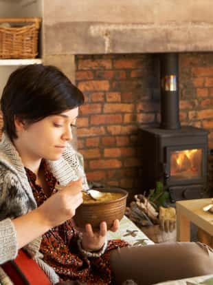 Young woman eating soup indoors sitting by fire